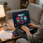 Engaging with SHBET casino games on a laptop while managing bankroll notes in a cozy home setting.