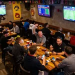 Engaged sports fans reviewing kèo nhà cái 5 odds in a lively sports bar atmosphere.