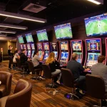Dynamic scene of sports enthusiasts betting on 1gom with screens displaying live games in a vibrant casino lounge.